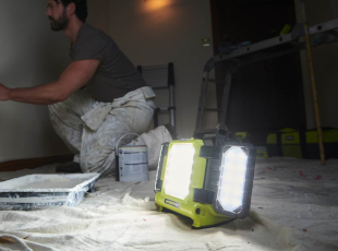 Ein Handwerker streicht eine Wand, während eine helle Arbeitsleuchte den Raum erhellt