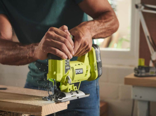 Eine Person benutzt eine grüne Stichsäge, um Holz zu schneiden