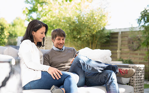 Ein Paar sitzt draußen auf einem Sofa und schaut auf ein Tablet