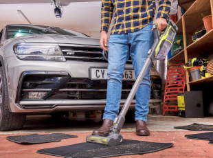 Eine Person saugt eine Fußmatte in einer Garage mit einem kabellosen Staubsauger ab