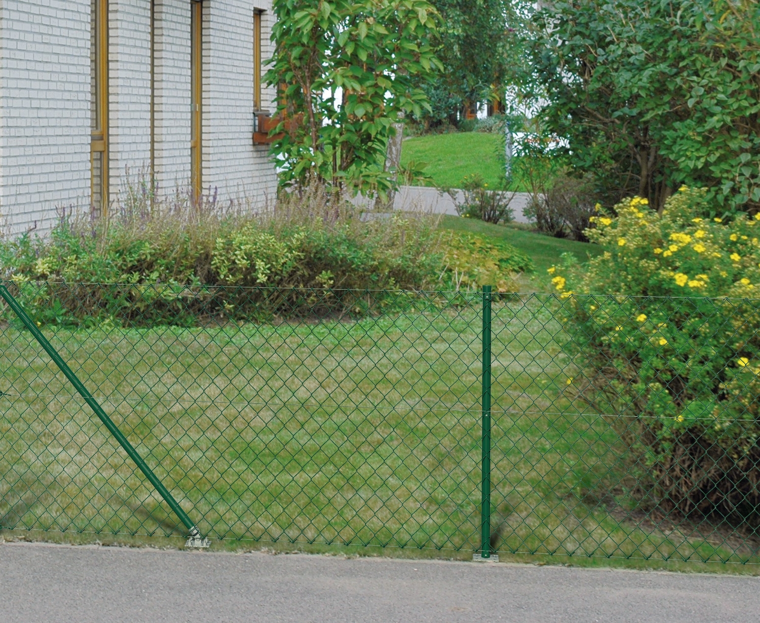 Ein grüner Maschendrahtzaun vor einem Gartengrundstück