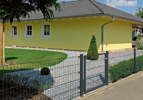 Gelbes Haus mit grauem Dach und Gartenweg aus Kies.