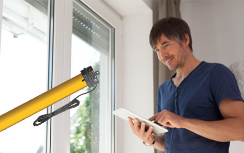 Ein Mann benutzt ein Tablet neben einem Fenster mit einem gelben elektrischen Rollladenmotor im Vordergrund