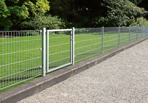 Metallzaun mit Tor vor einer Rasenfläche und einem Kiesweg