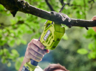 Person schneidet Ast mit einer elektrischen Säge ab