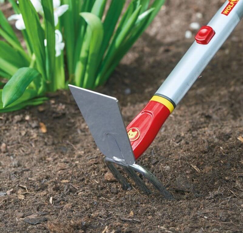 Gartenwerkzeug mit Hacke und Gabel im Boden vor Pflanzen