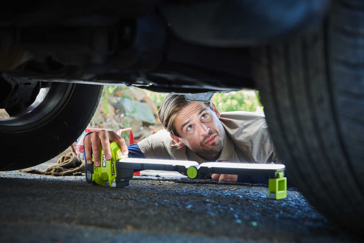 Ein Mann inspiziert den Unterboden eines Autos mit einer Lampe