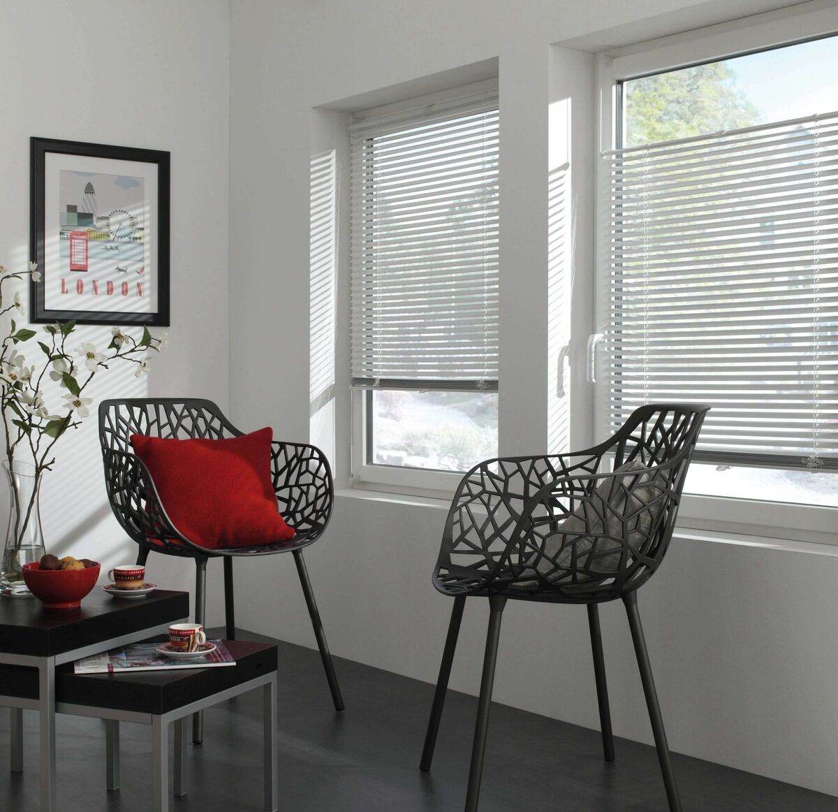 Zwei schwarze Stühle mit roten Kissen stehen in einem hellen Raum mit Jalousien an den Fenstern