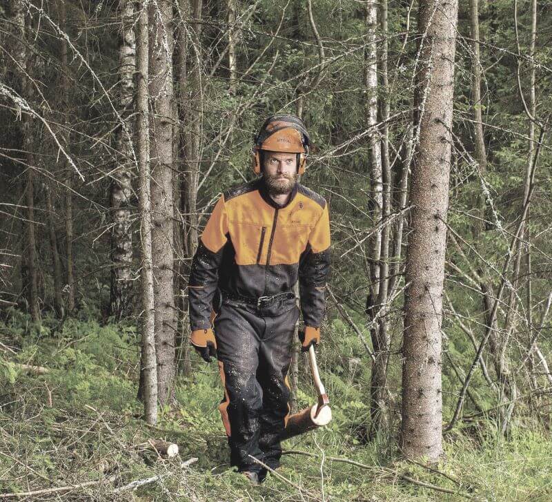 Ein Mann in Schutzkleidung mit Axt geht durch einen Wald