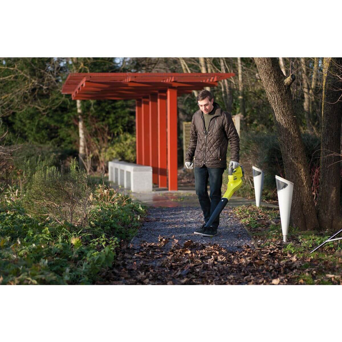 Ein Mann benutzt einen Laubbläser auf einem Gartenweg