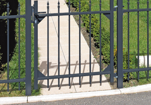 Ein schwarzes Metalltor mit senkrechten Stäben vor einem gepflasterten Weg