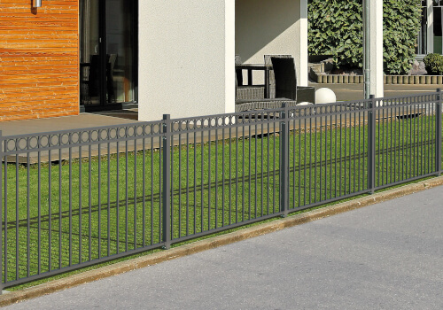 Ein moderner Metallzaun trennt einen Rasen von einem Gehweg