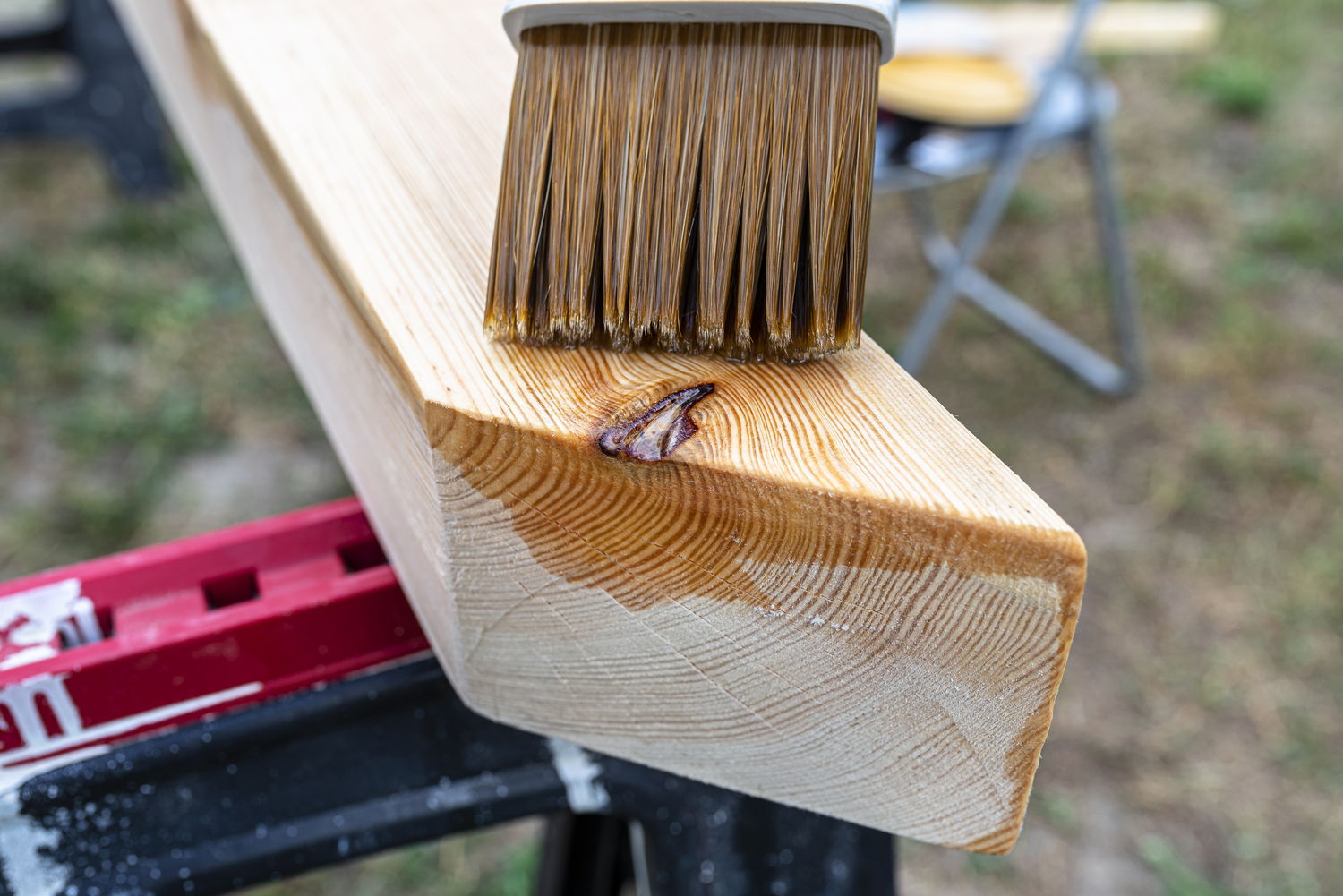 Ein Pinsel trägt Holzschutzmittel auf einen Holzbalken auf