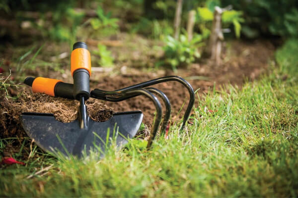 Gartenwerkzeuge liegen auf dem Rasen vor einem Beet