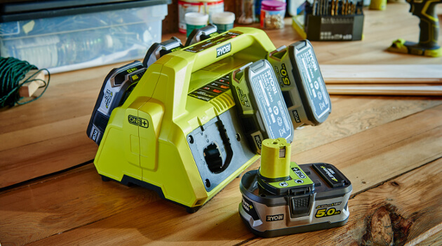 Ein grünes Ladegerät mit mehreren Akkus auf einer Werkbank